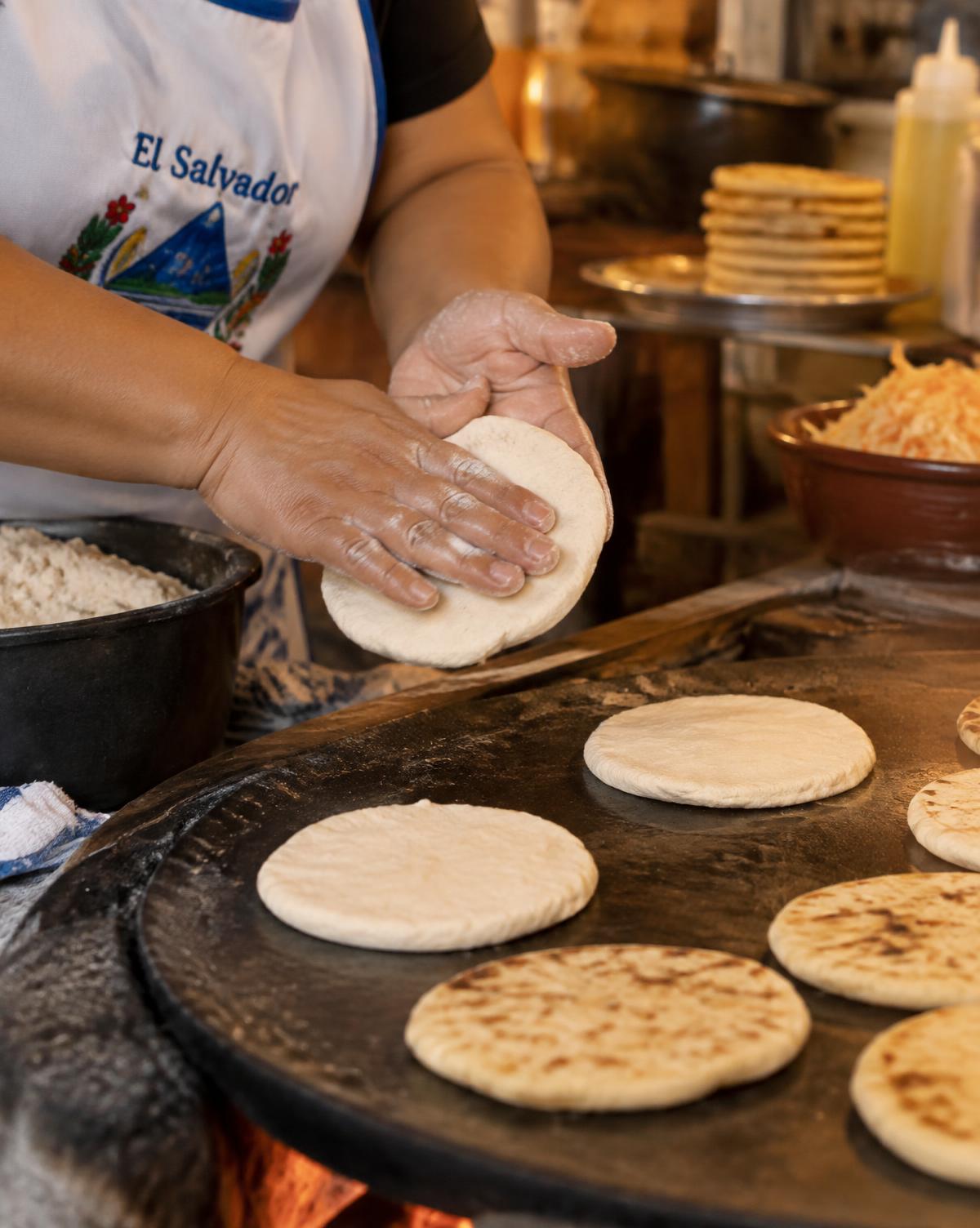 Cook shaping masa by hand for pupusas on a hot comal